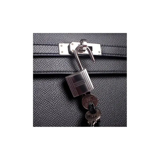 Hermès Kelly 25 handbag padlock and keys in silver on black leather, showcasing luxury bag details and craftsmanship.