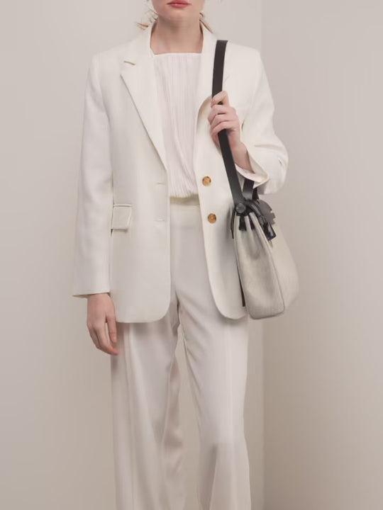 Stylish woman in a white suit holding a designer black and gray handbag, perfect for a trendy fashion statement.